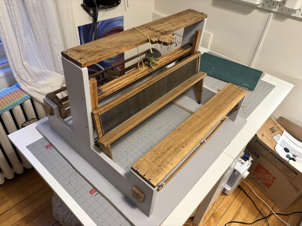 a secondhand loom, on my sewing table. It's bits of an antique loom, mounted on grey-painted plywood.