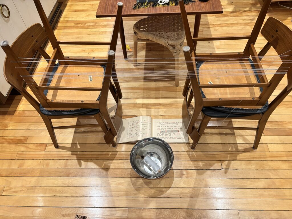 A picture of my warp-winding setup-- two inverted chairs with the legs sticking up to use as pegs. A silver bowl on the floor holds my yarn.