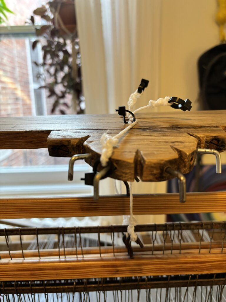 Nylon cords with loops made of zip ties, attached to the shafts of the loom. The second shaft is held in a raised position by its cord, which is looped around a hook.