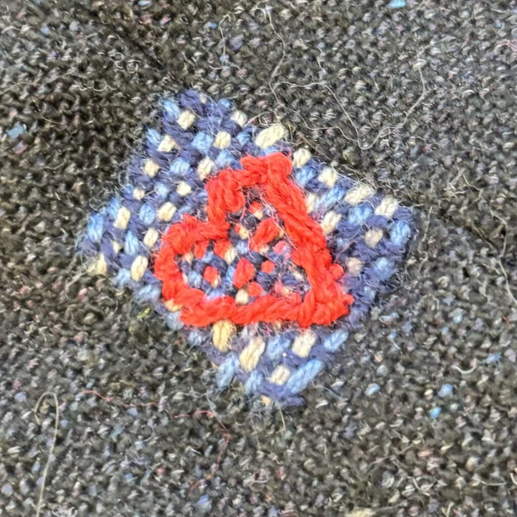 A messy plain weave patch in wedgewood, navy and greige, with a red heart both worn and embroidered